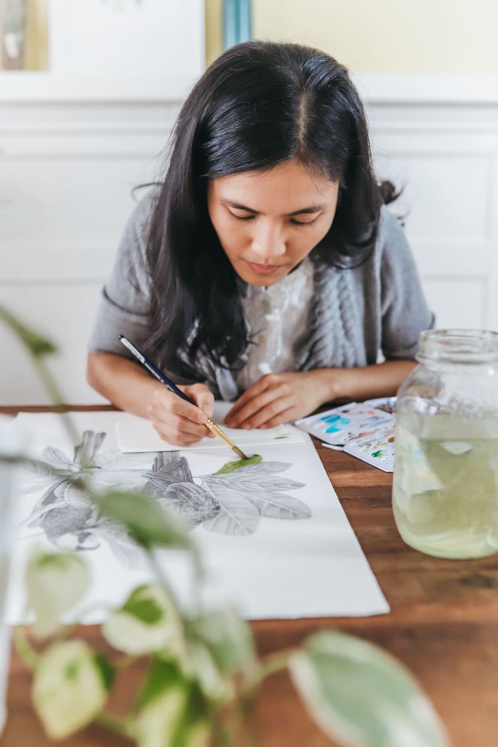 Stacy Hsu painting watercolour washes over a pencil rendering of sloths at her desk